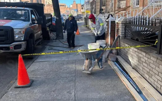 Workers finishing a concrete sidewalk in front of brick row houses with a truck at the curb, sidewalk repair by Sidewalk Repair Near Me in NYC