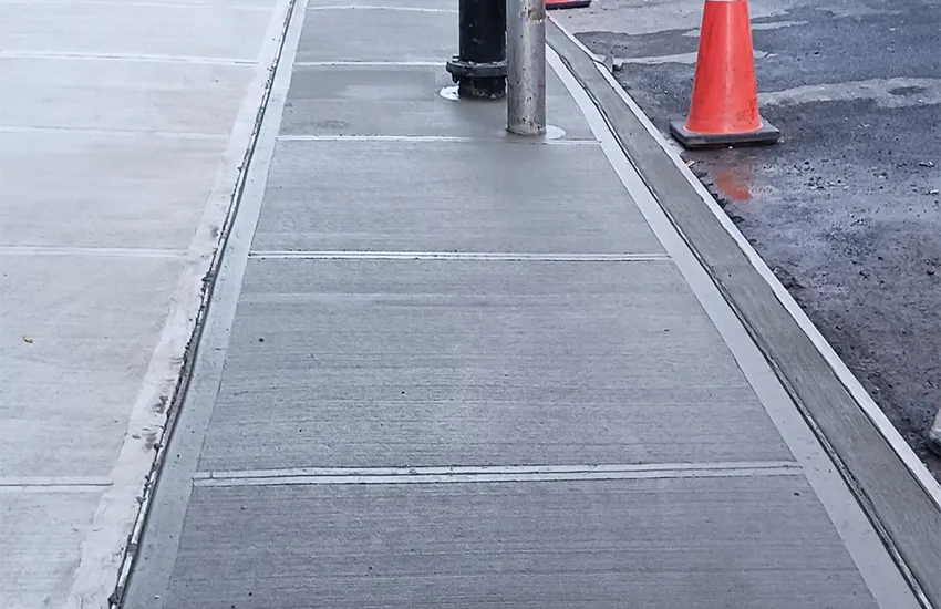 New concrete sidewalk and curb along a New York City street with a safety cone, sidewalk repair by Sidewalk Repair Near Me in NYC