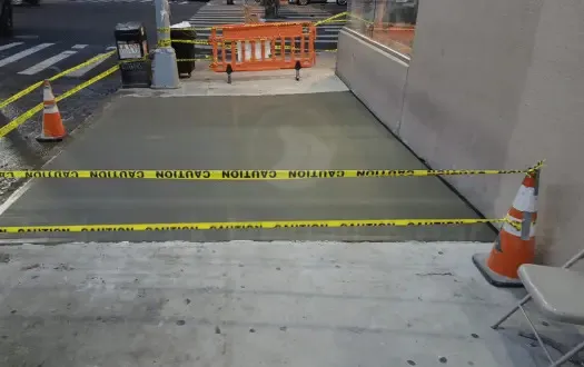 New concrete sidewalk wrapping the corner of a building, taped off with caution tape, as on many Manhattan corner lots