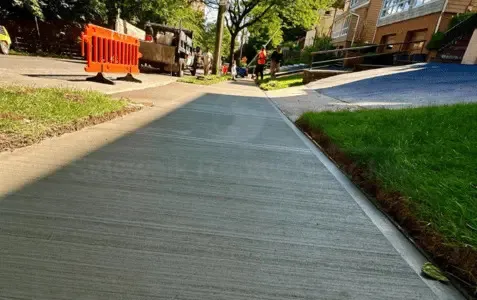 Newly poured concrete sidewalk along a residential block with a lawn edge, like many house blocks in Queens