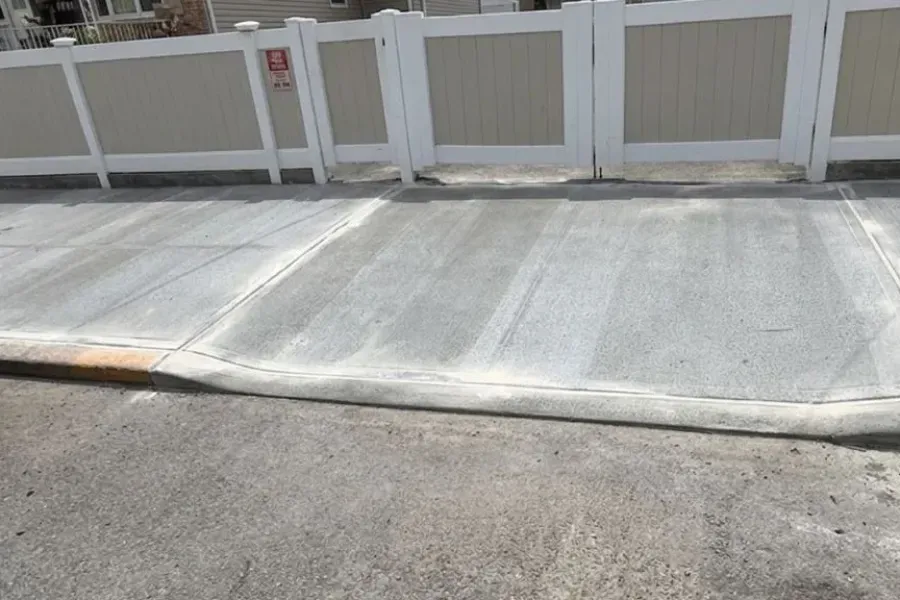 New concrete sidewalk and curb cut in front of a white fence in Queens after repair, sidewalk repair by Sidewalk Repair Near Me in NYC