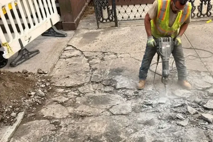 Worker breaking out damaged concrete with a jackhammer for a violation repair in Brooklyn, sidewalk repair by Sidewalk Repair Near Me in NYC