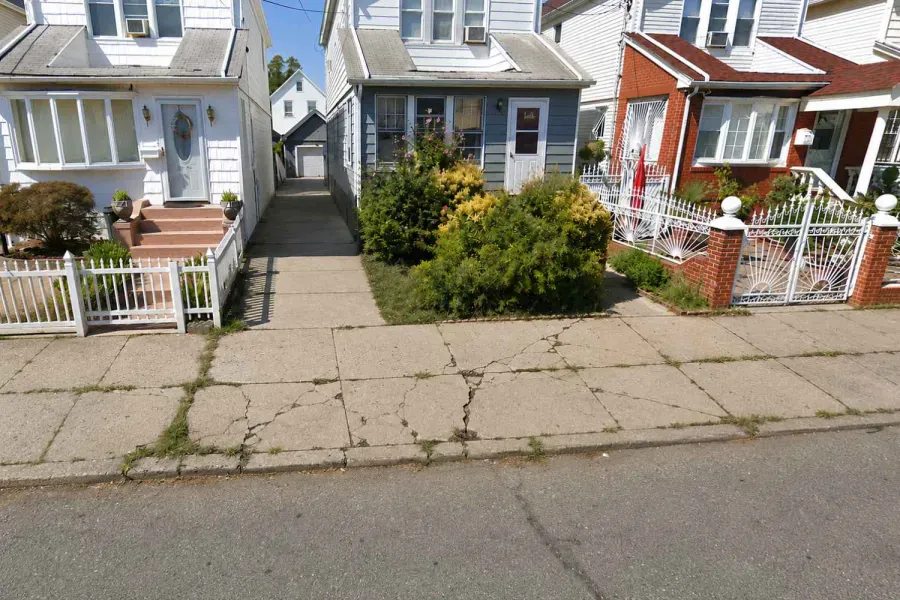 Before: Cracked sidewalk in front of detached homes in Jamaica Hills, Queens before repair