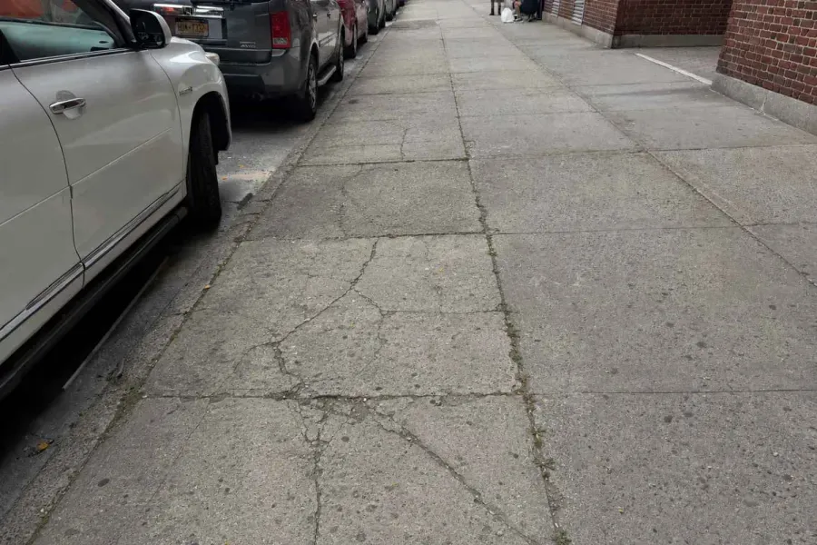 Before: Cracked sidewalk beside a brick rental building in Sunnyside, Queens before repair