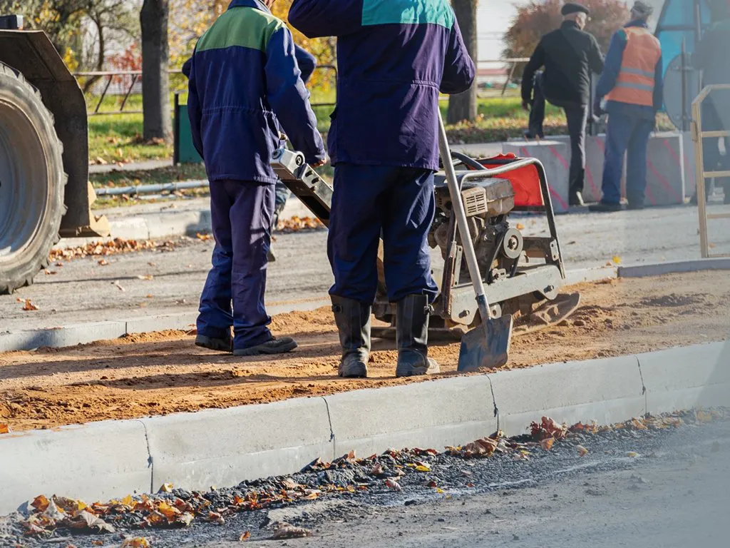 Crew compacting the base beside a newly set concrete curb, concrete work by Sidewalk Repair Near Me in NYC
