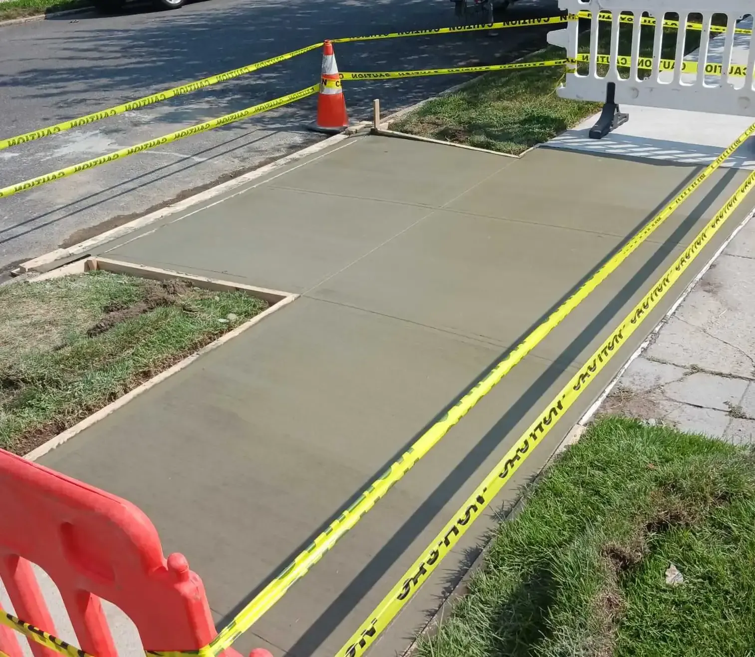 Fresh concrete sidewalk section taped off beside a lawn, concrete work by Sidewalk Repair Near Me in NYC