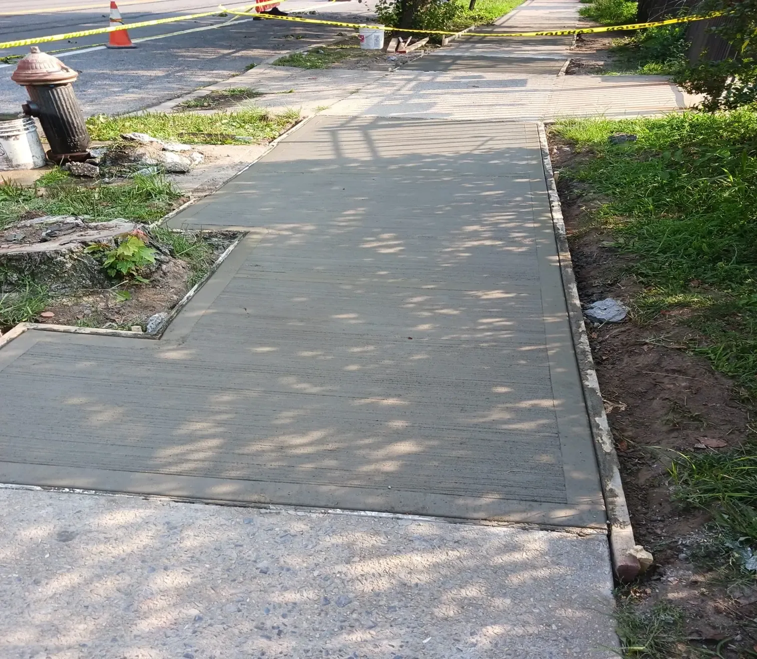 Fresh concrete sidewalk poured around a lawn corner, concrete work by Sidewalk Repair Near Me in NYC