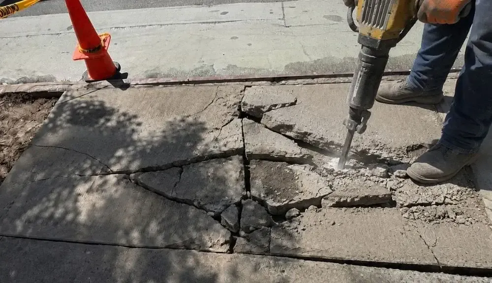 Worker breaking up cracked sidewalk concrete with a jackhammer