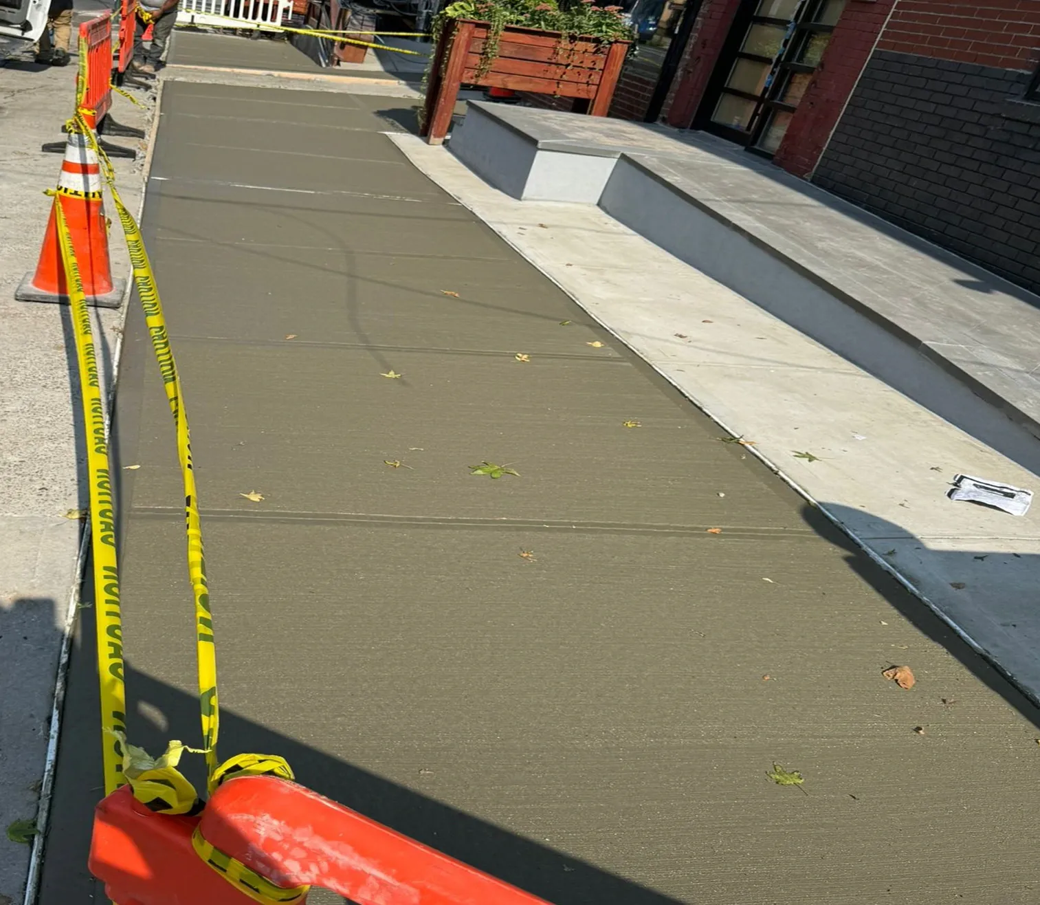 Long run of fresh concrete sidewalk with cones and caution tape, concrete work by Sidewalk Repair Near Me in NYC