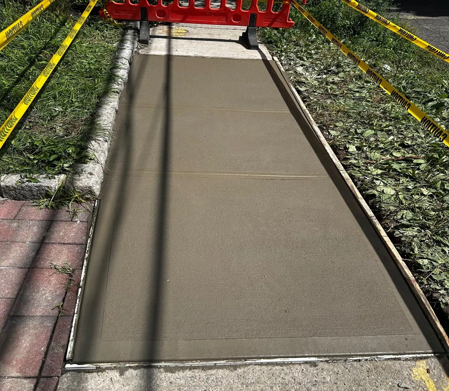 New concrete walkway strip formed between a lawn and brick pavers, concrete work by Sidewalk Repair Near Me in NYC