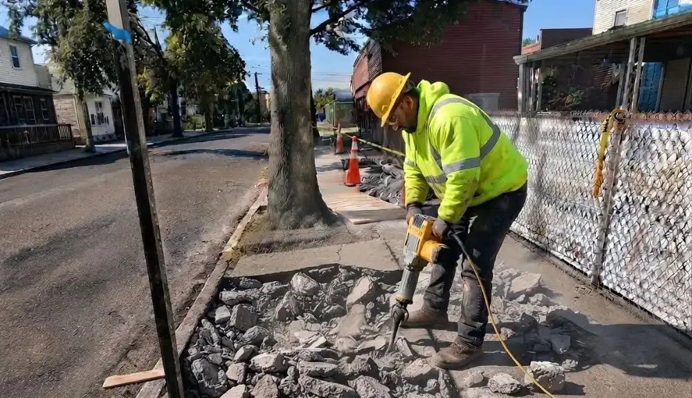 Worker breaking out a root damaged sidewalk beside a street tree in the Bronx, concrete work by Sidewalk Repair Near Me in NYC