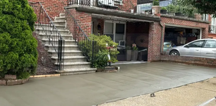 Fresh concrete driveway in front of a brick house with entry steps and iron railings, concrete driveway work by Sidewalk Repair Near Me in NYC