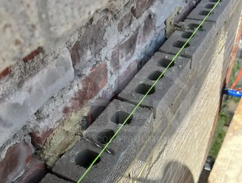 New block course set to a string line against an old brick wall, masonry work by Sidewalk Repair Near Me in NYC