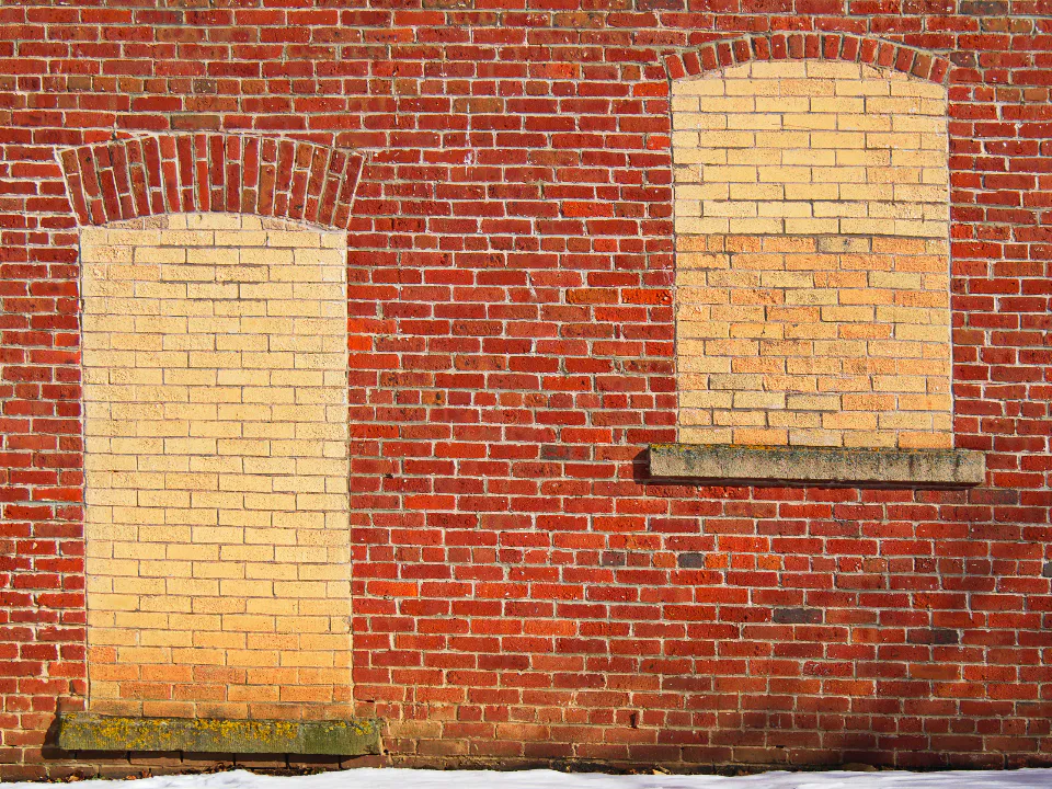 Brick wall with two window openings filled in with lighter brick