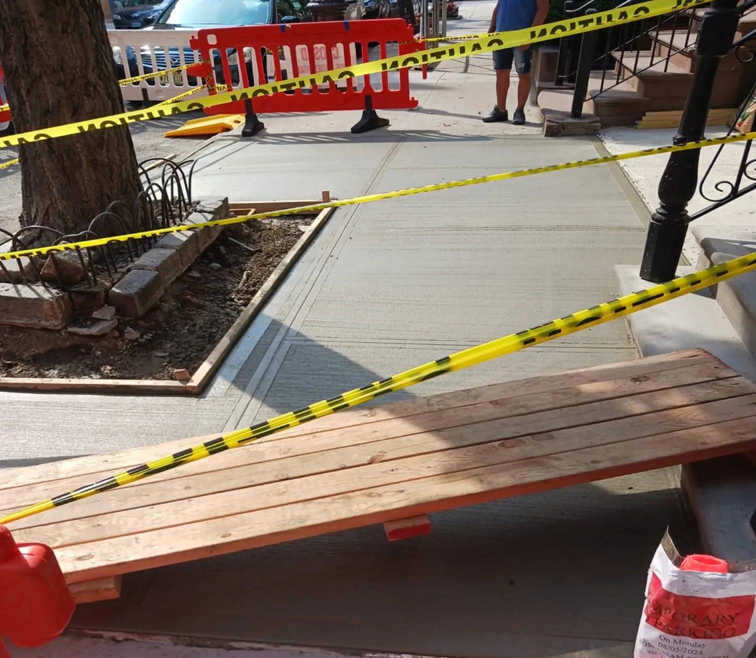 Fresh concrete around a tree pit, taped off with a wooden walkway board, sidewalk repair by Sidewalk Repair Near Me in NYC
