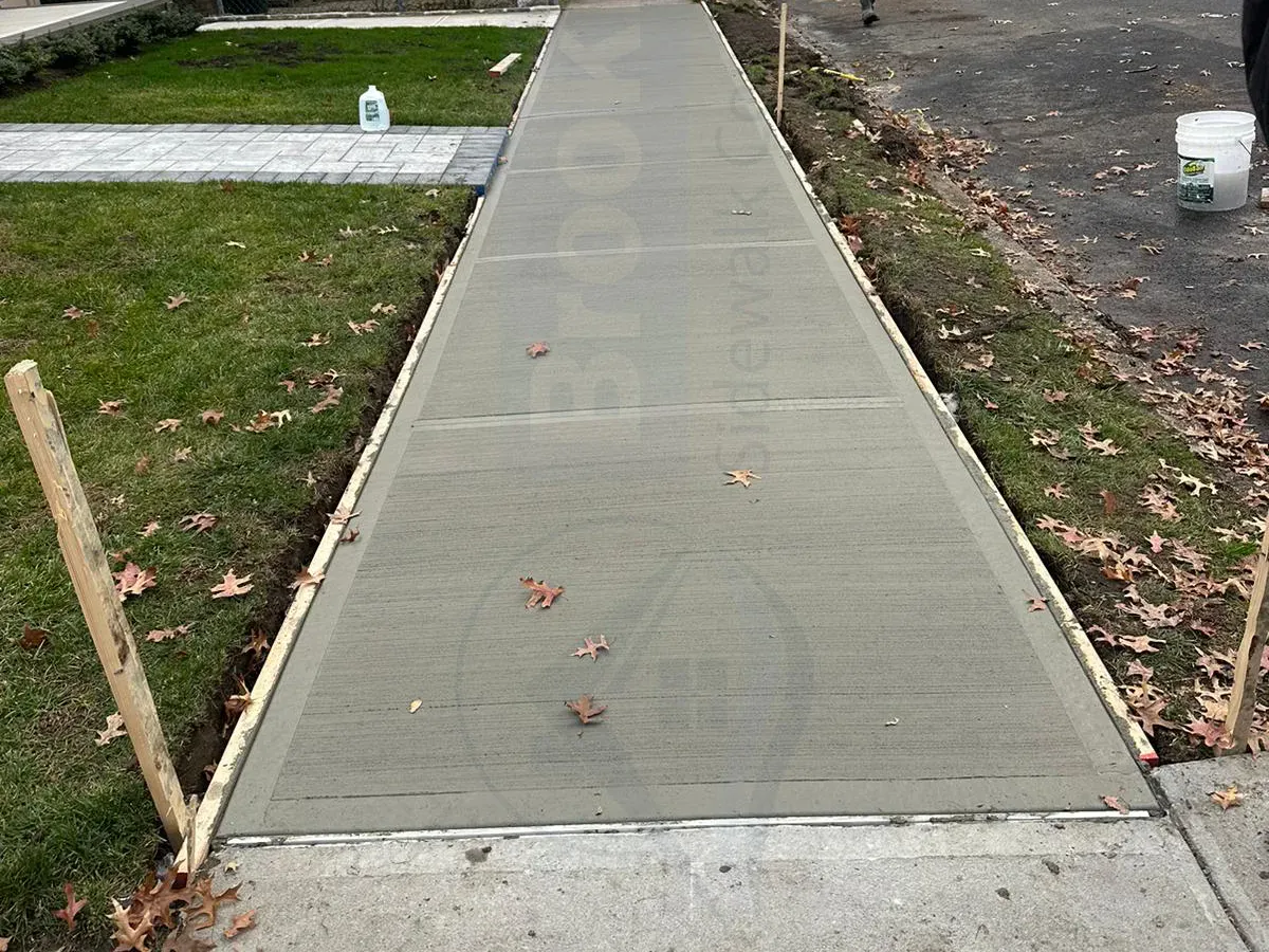 Fresh concrete sidewalk strip between lawns on a residential street, sidewalk repair by Sidewalk Repair Near Me in NYC