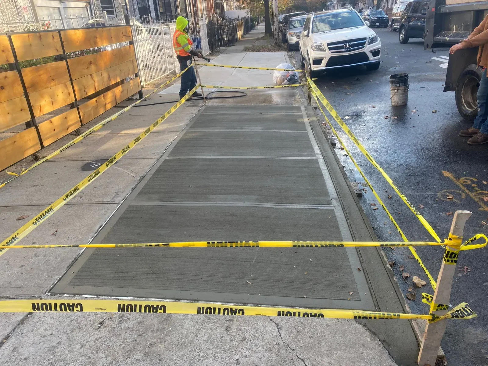 Freshly poured sidewalk strip taped off between a wood fence and the street, sidewalk repair by Sidewalk Repair Near Me in NYC