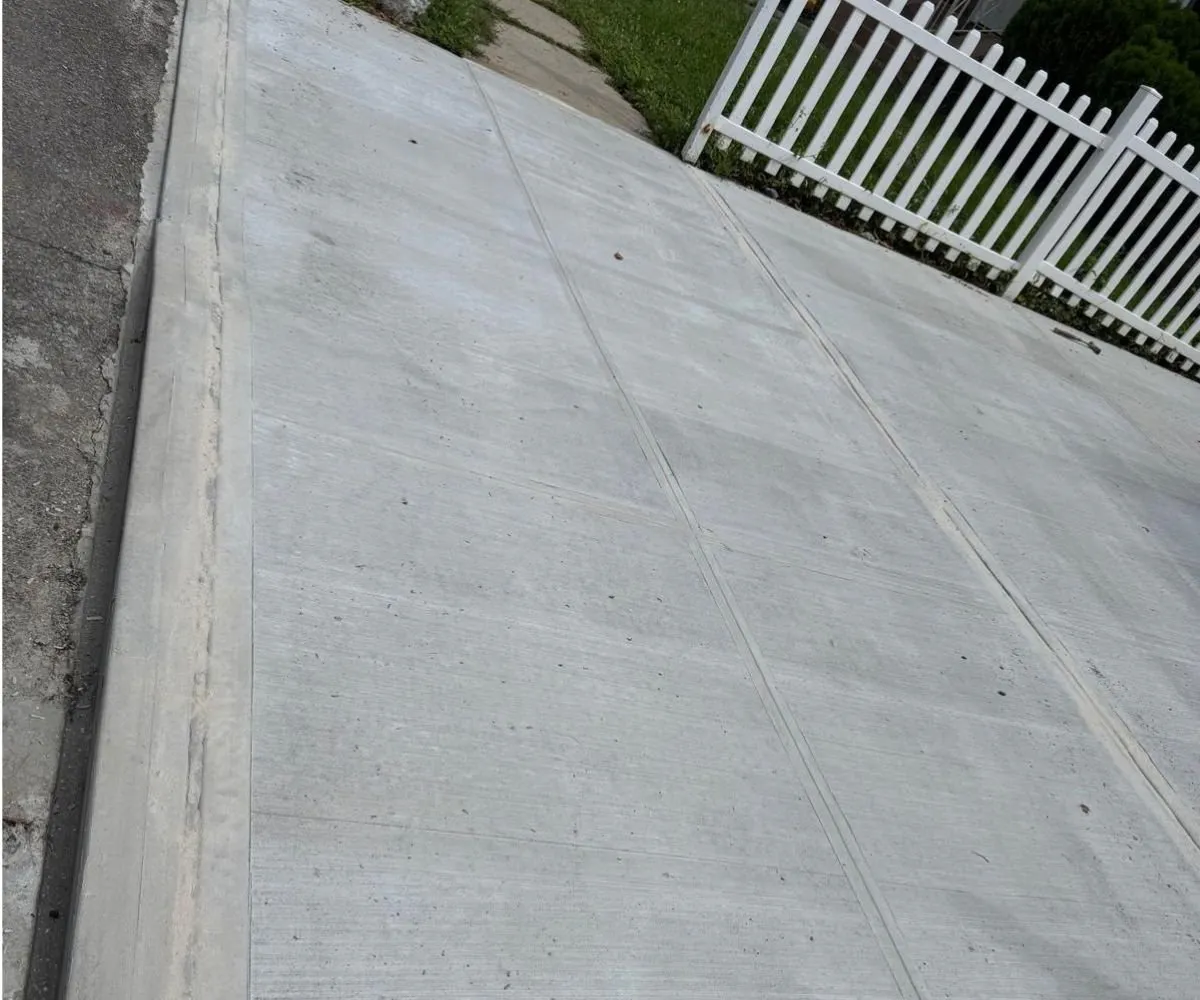 New concrete sidewalk flags beside a white picket fence, sidewalk repair by Sidewalk Repair Near Me in NYC
