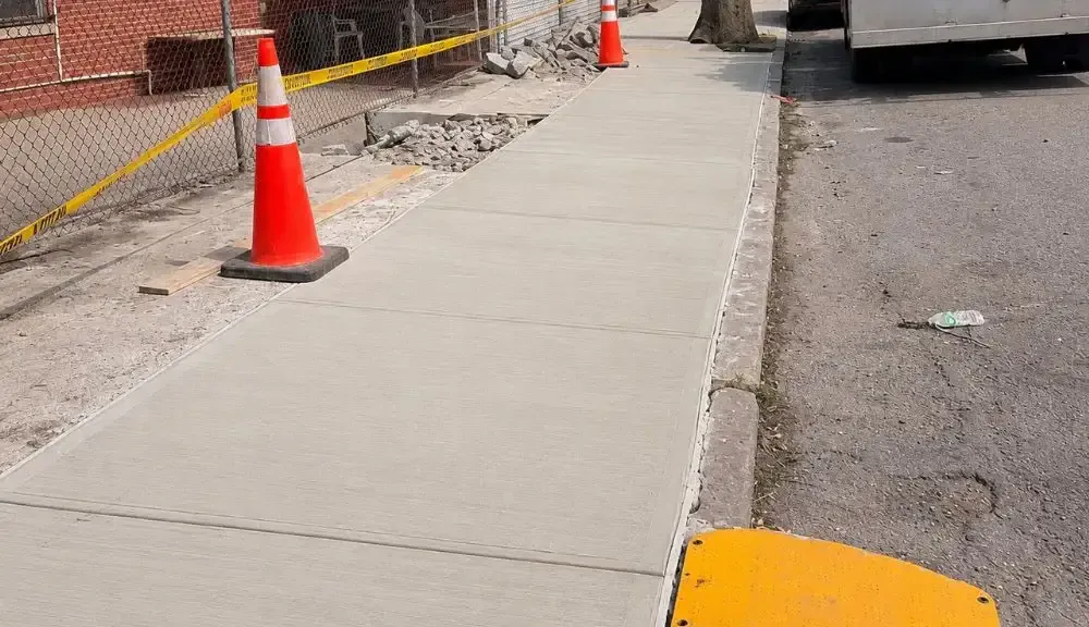 New concrete sidewalk along the curb with a cone and caution tape, sidewalk repair by Sidewalk Repair Near Me in NYC