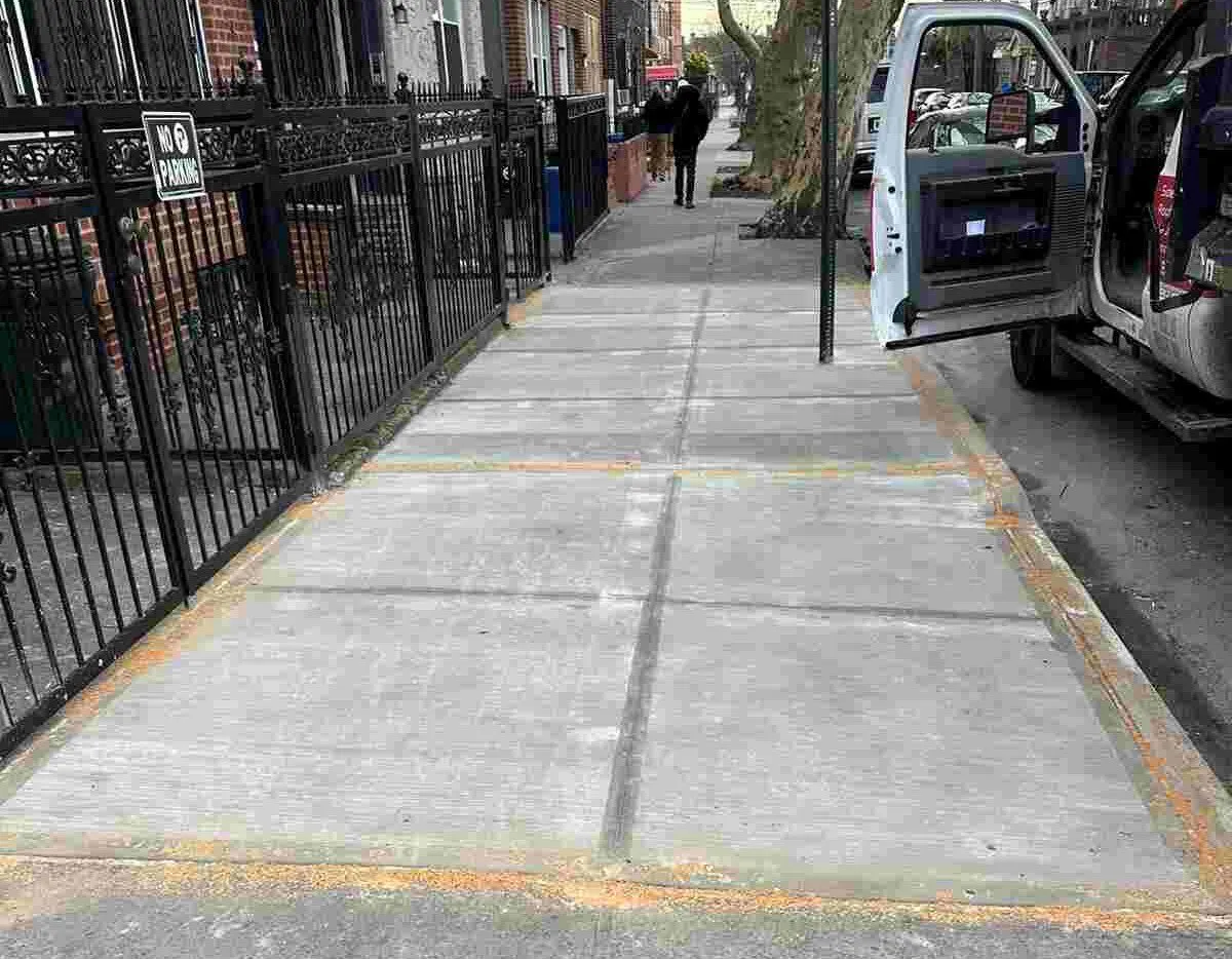 New concrete sidewalk flags beside a black iron fence, sidewalk repair by Sidewalk Repair Near Me in NYC