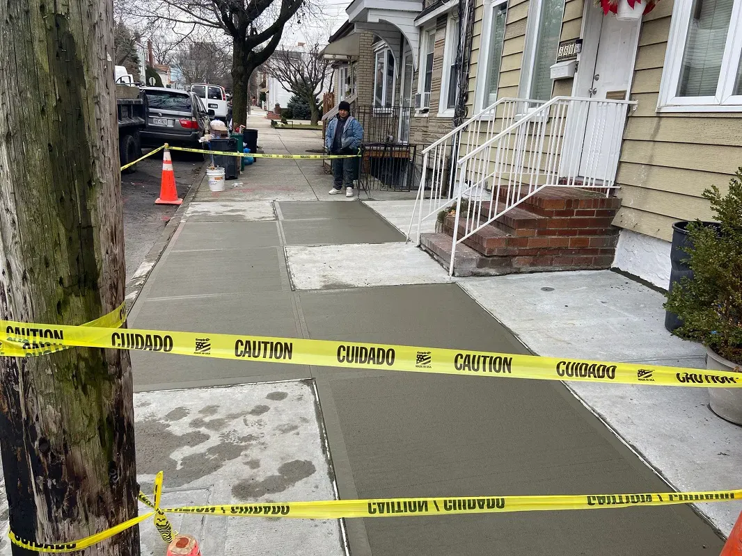 New sidewalk flags taped off in front of frame houses with brick steps, sidewalk repair by Sidewalk Repair Near Me in NYC