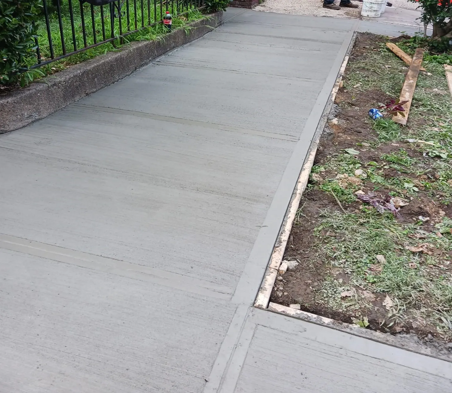 New concrete sidewalk beside a low wall and an iron fence, sidewalk repair by Sidewalk Repair Near Me in NYC