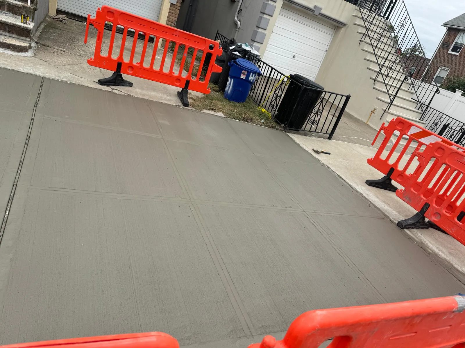 Wide section of fresh concrete sidewalk with orange barriers around it, sidewalk repair by Sidewalk Repair Near Me in NYC