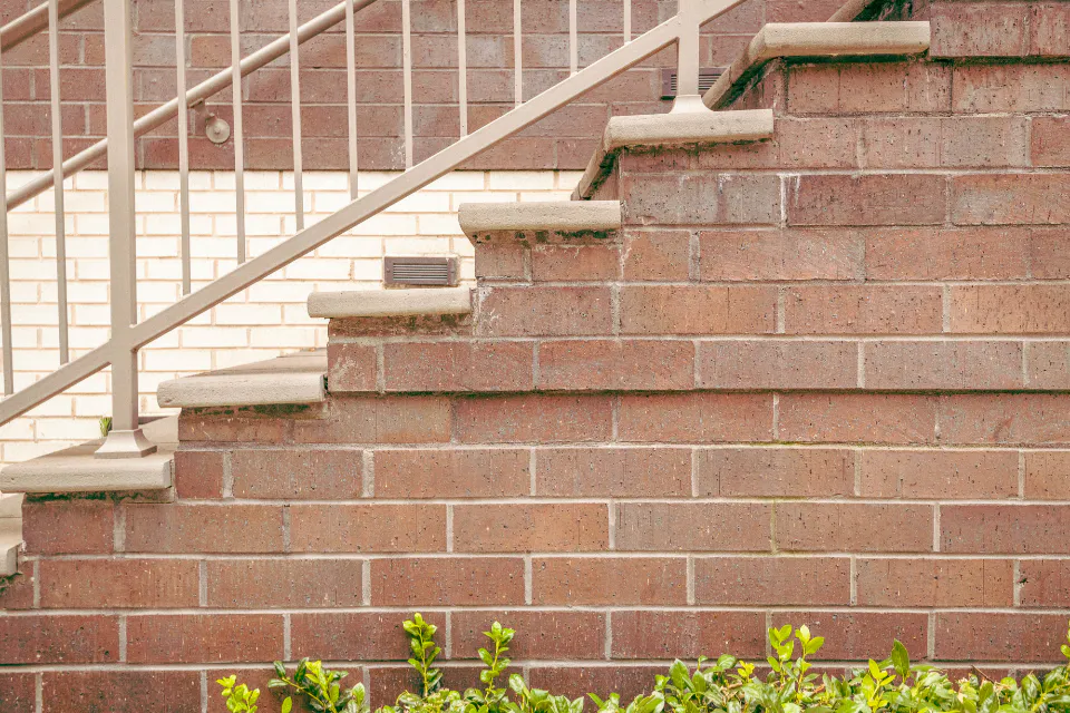 Brick stair wall with stone caps and a white metal railing