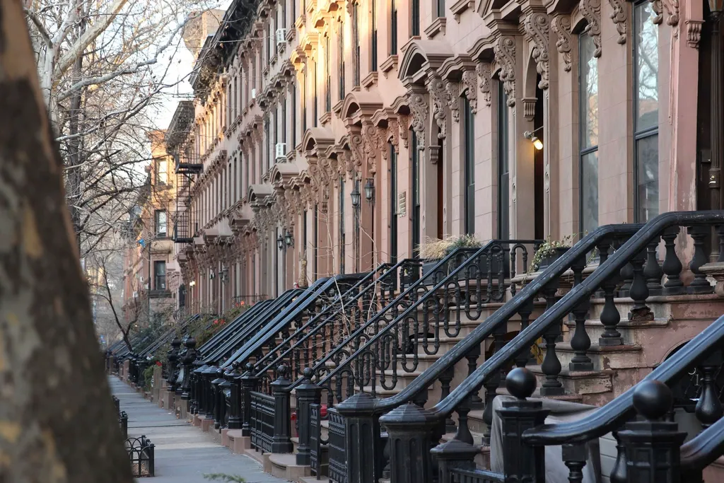 Row of brownstone stoops with iron railings along a city sidewalk