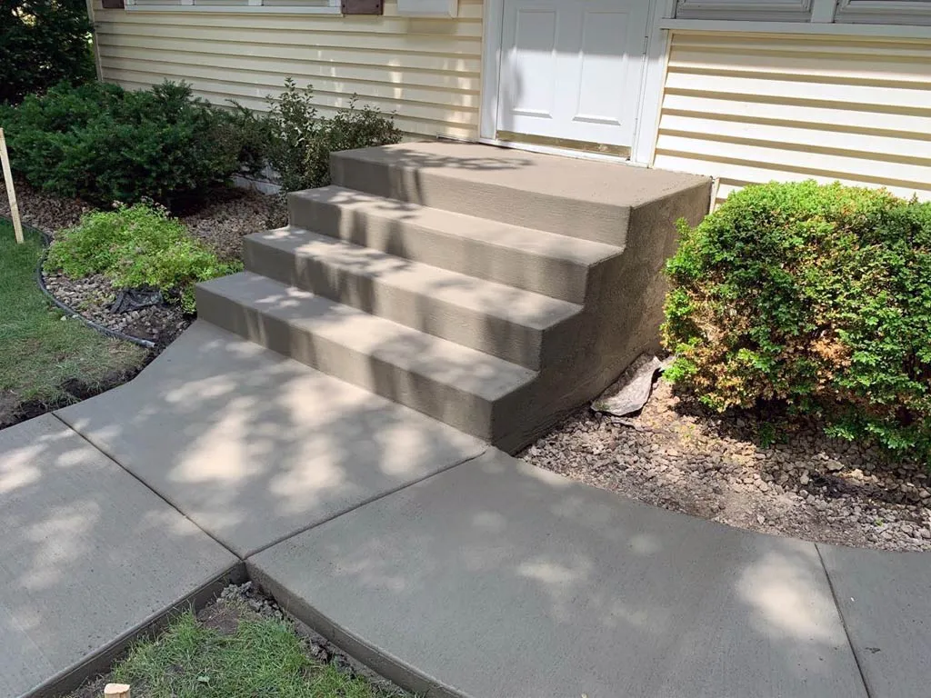 Concrete steps next to a concrete walkway and shrubs, steps and stoop repair by Sidewalk Repair Near Me in NYC