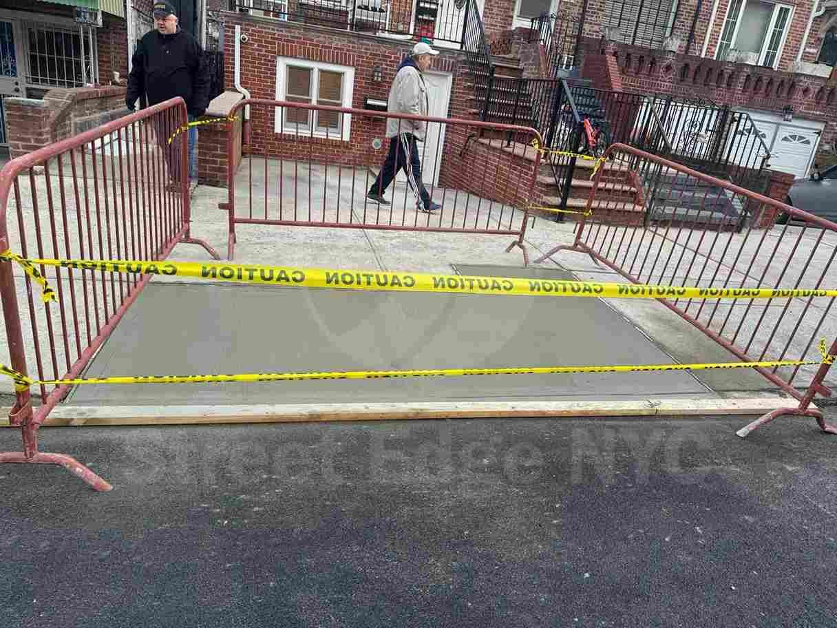 Yellow-painted curb cut with accessible wheelchair markings on a sidewalk, showing a designated ramp for accessibility compliance.